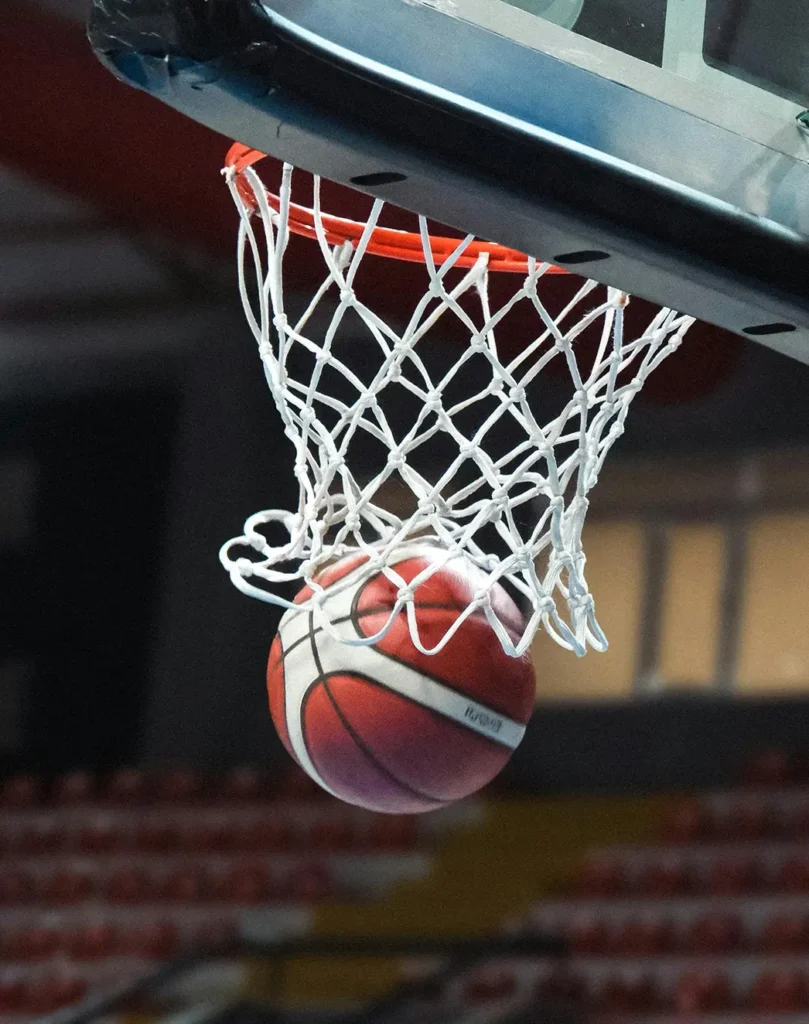 Gros plan sur un ballon de basket qui passe à travers le cerceau et le filet pendant un match, immortalisant le moment du panier dans une salle omnisports.