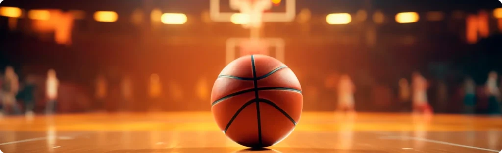 Un ballon de basket posé sur un terrain, sous les lumières chaudes de la salle, avec des joueurs flous en arrière-plan, symbolisant la concentration avant un match.